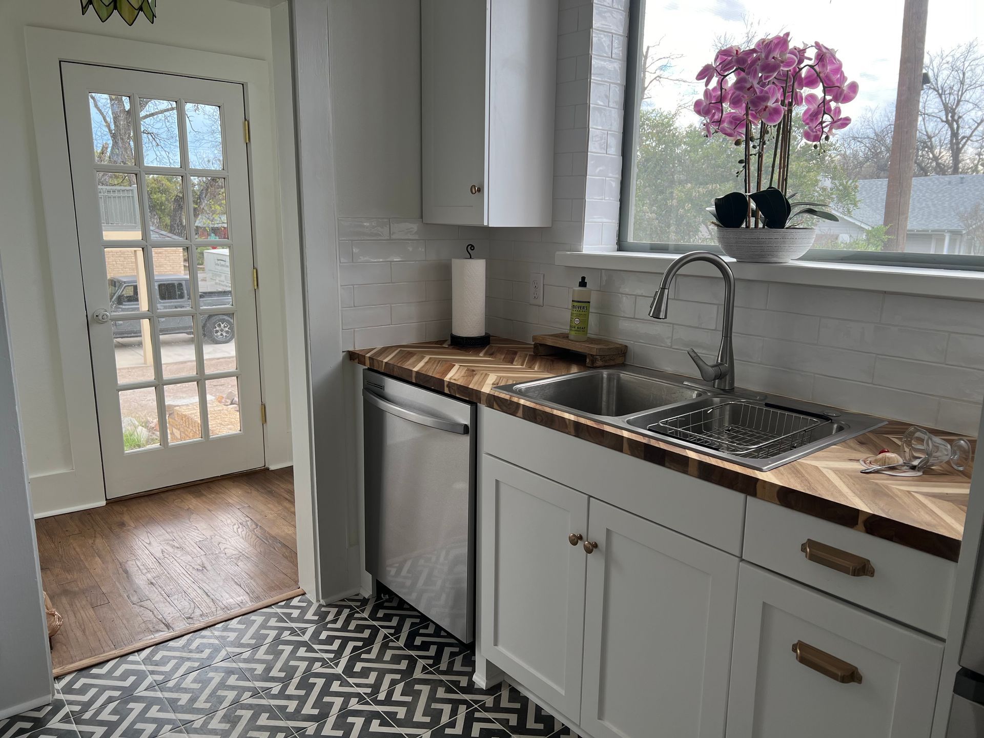 Kitchen with white cabinets, stainless steel appliances, wood countertops, and a double sink. A French door leads outside.
