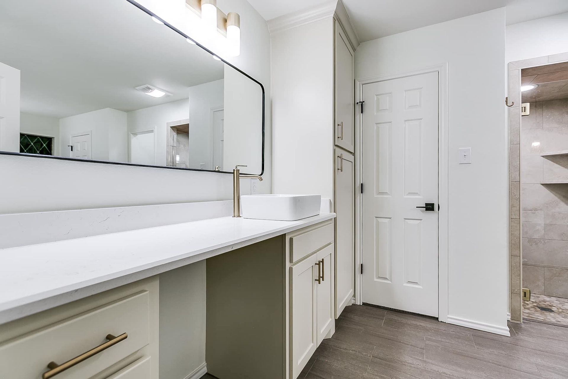 White bathroom with long mirror, vanity, storage, and shower.