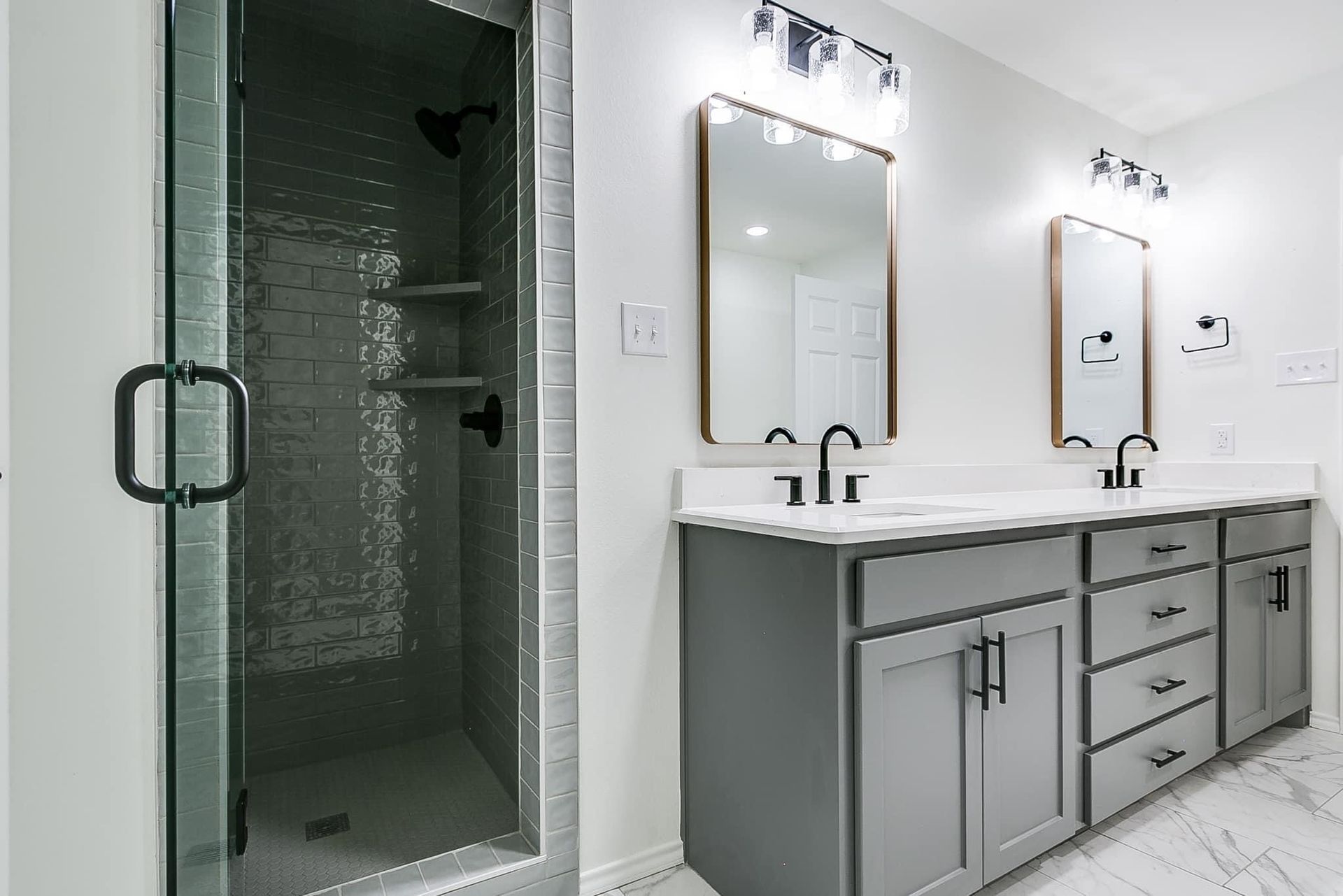 Modern bathroom with gray vanity, two sinks, shower, and mirrors. White walls, gray cabinets, and black fixtures.