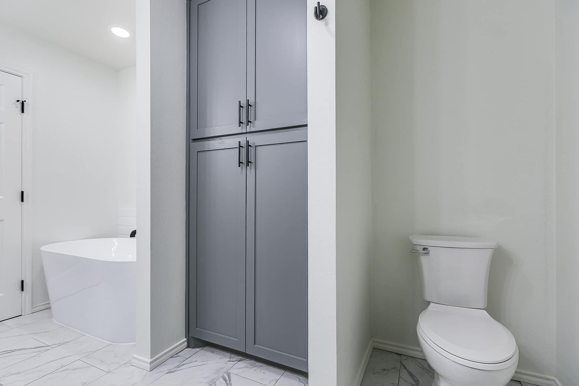 Bathroom with a gray storage cabinet, white toilet, and freestanding tub.