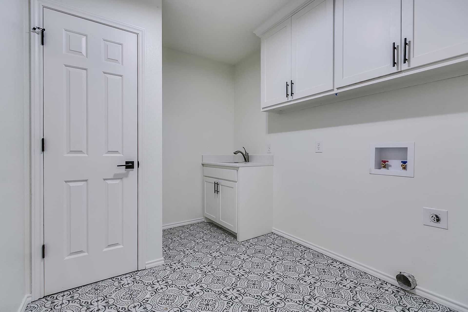 Laundry room with white cabinets, sink, patterned floor, and a door.