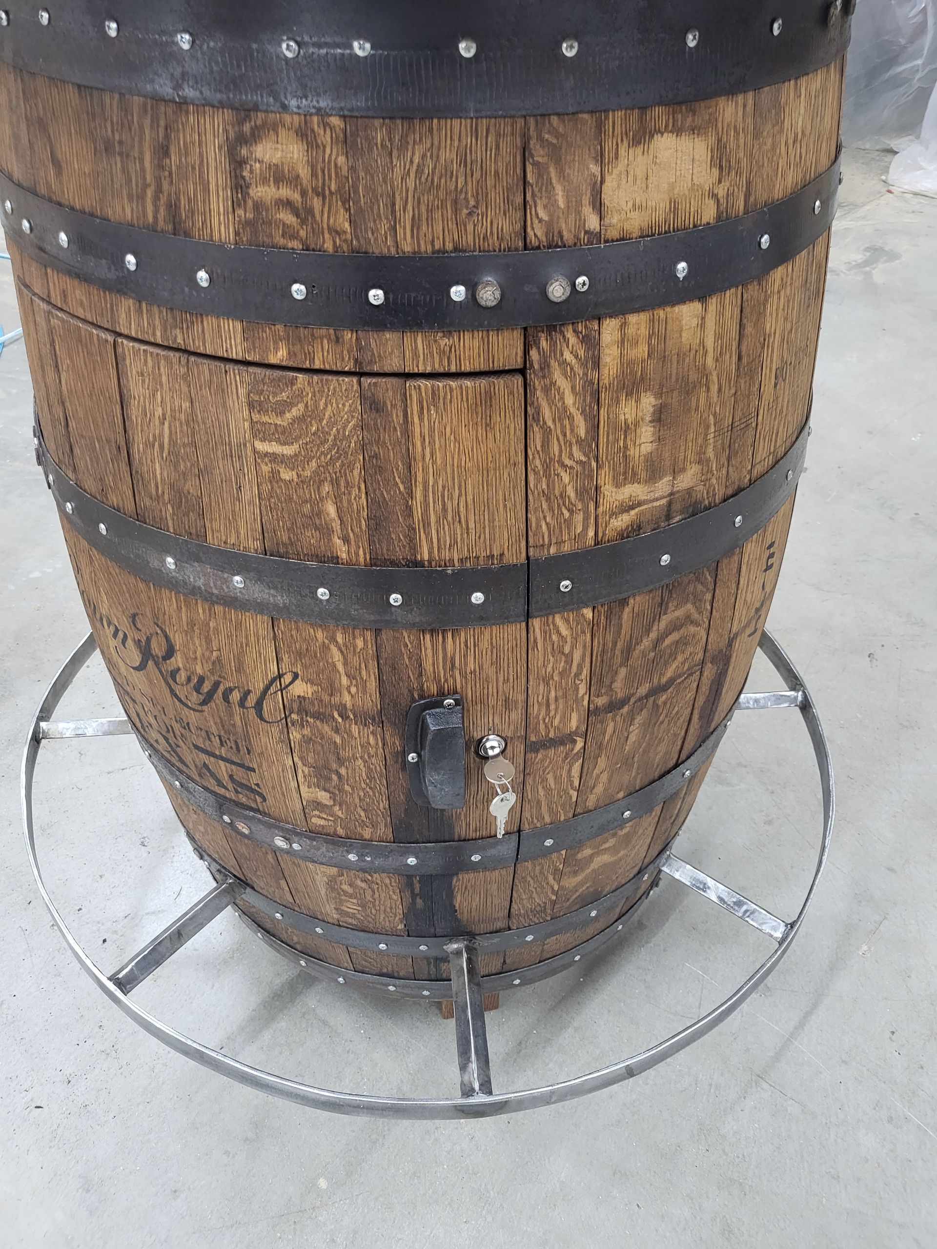 Wooden whiskey barrel with metal bands and door. Mounted on a metal base.