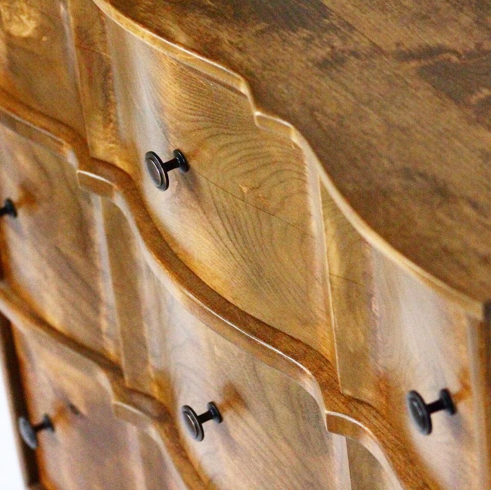 Wooden dresser with curved drawers and black knobs.