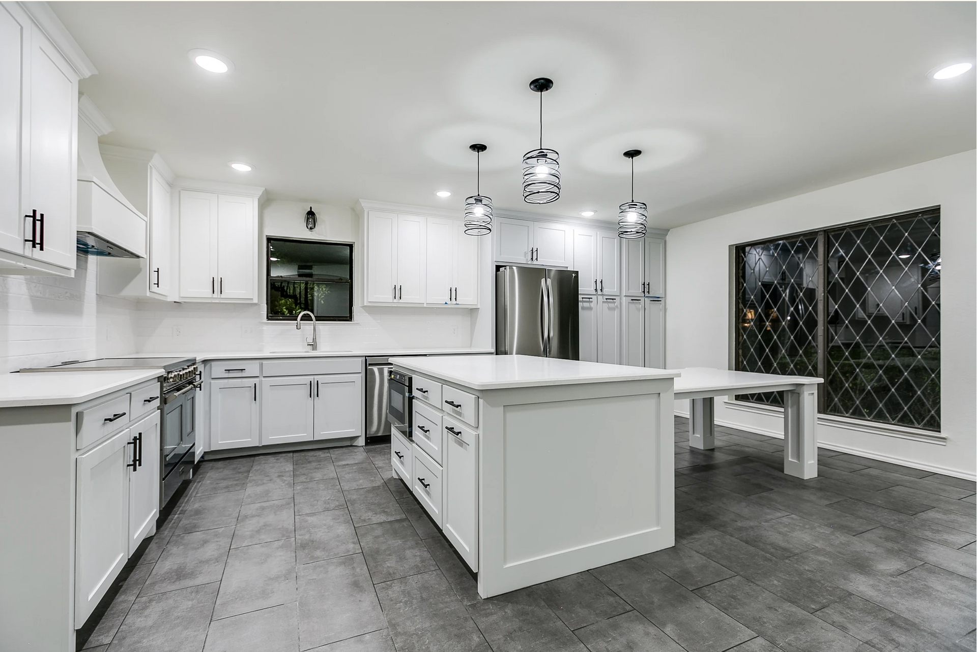 Bright white modern kitchen with island, stainless steel appliances, and large sliding glass door.