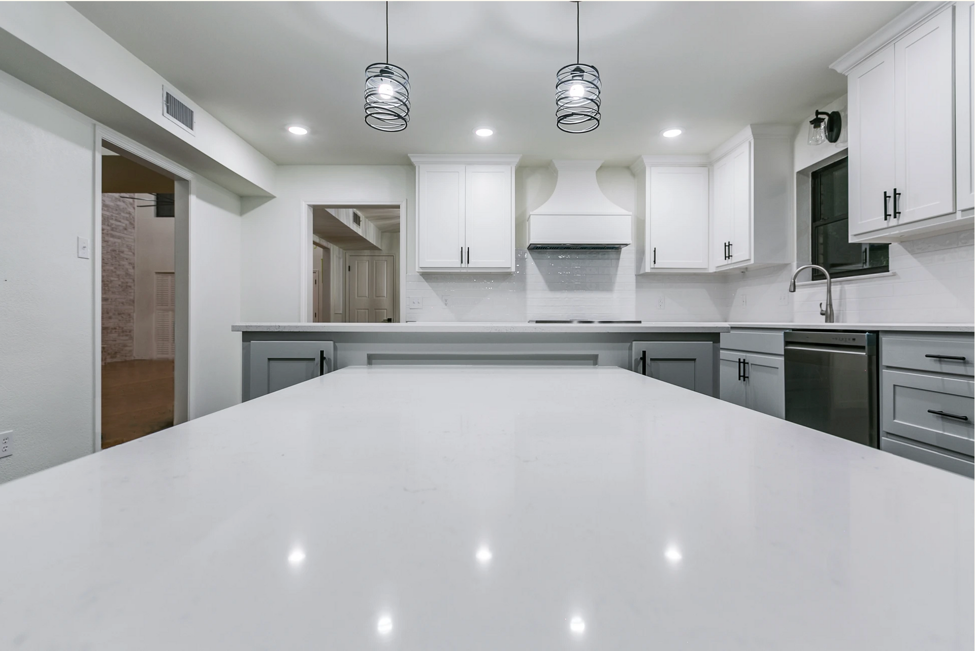 Modern white kitchen with island, gray cabinets, stainless steel appliances, and two pendant lights.