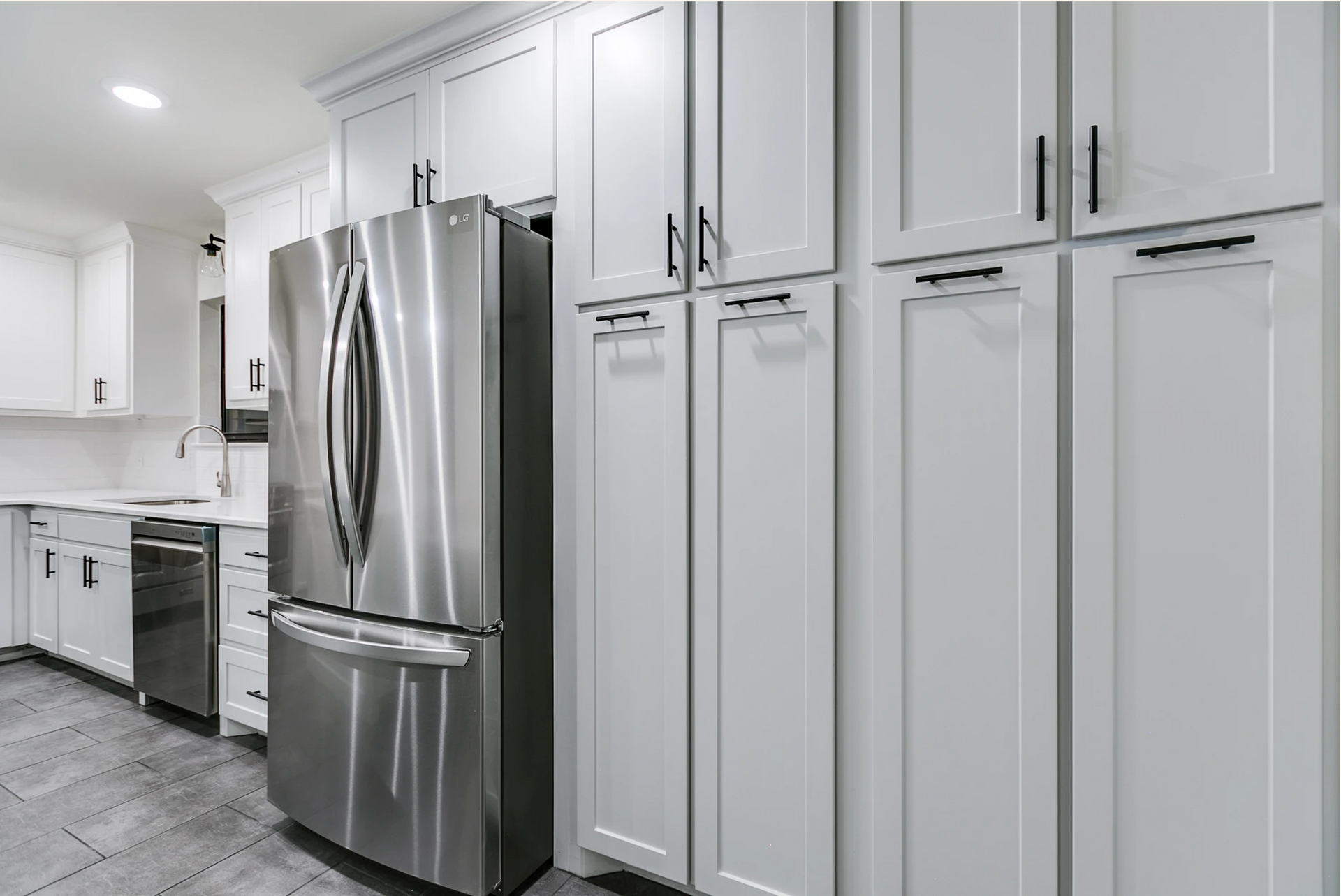 Stainless steel refrigerator next to white cabinets with black handles in a kitchen.