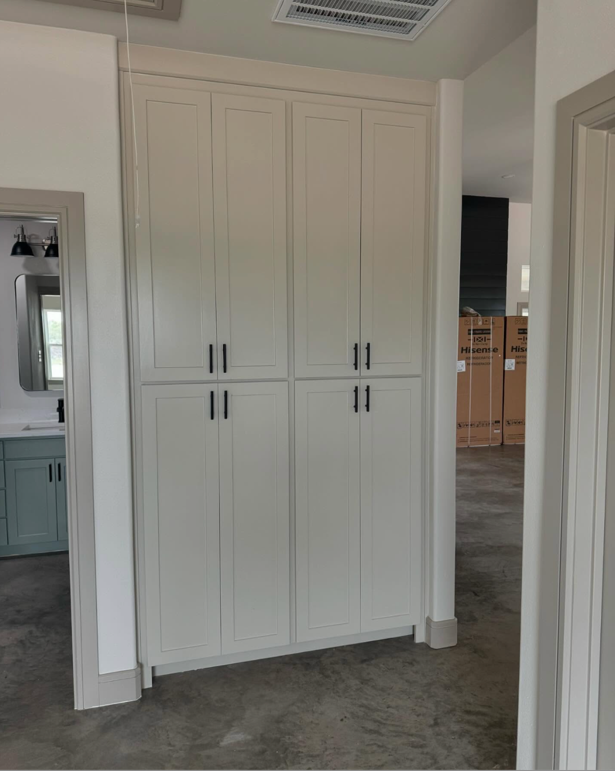 Tall, light gray cabinet with black handles in a hallway, near a bathroom.
