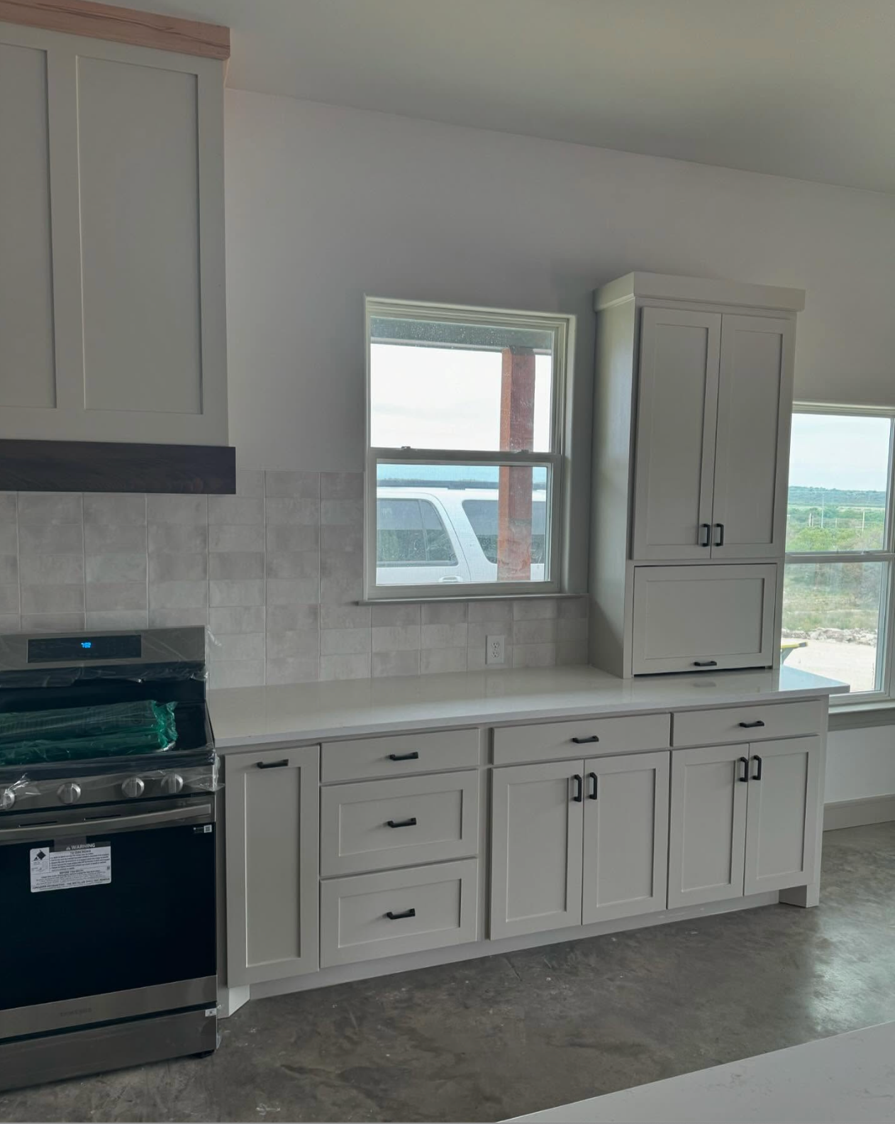 Kitchen with white cabinets, light countertops, and a stove. A window is in the background.