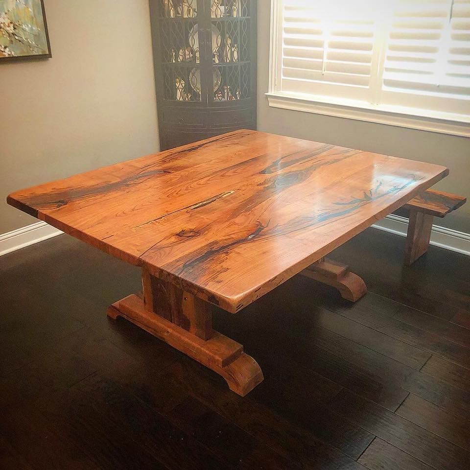 Wooden dining table with pedestal base in a room with a dark wooden floor and a window.