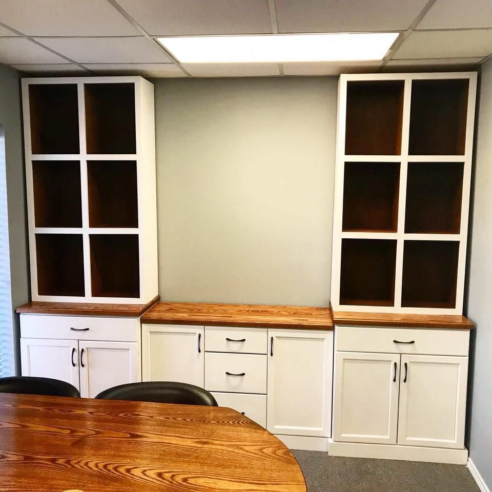 Built-in white cabinets with open shelves and a wooden countertop, in a room with a round wooden table.