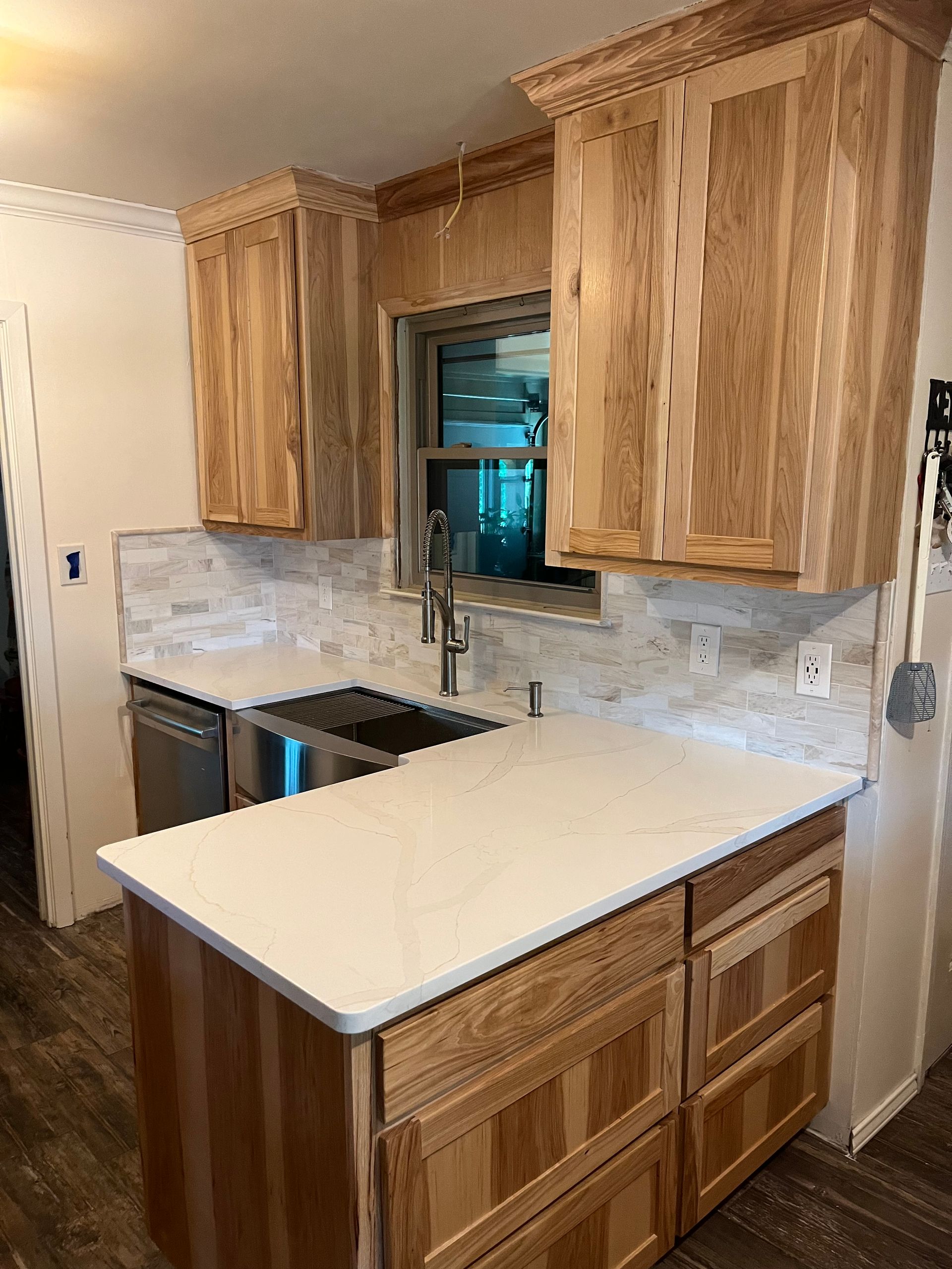 Wooden kitchen cabinets with white countertops and backsplash. Stainless steel sink and appliances.