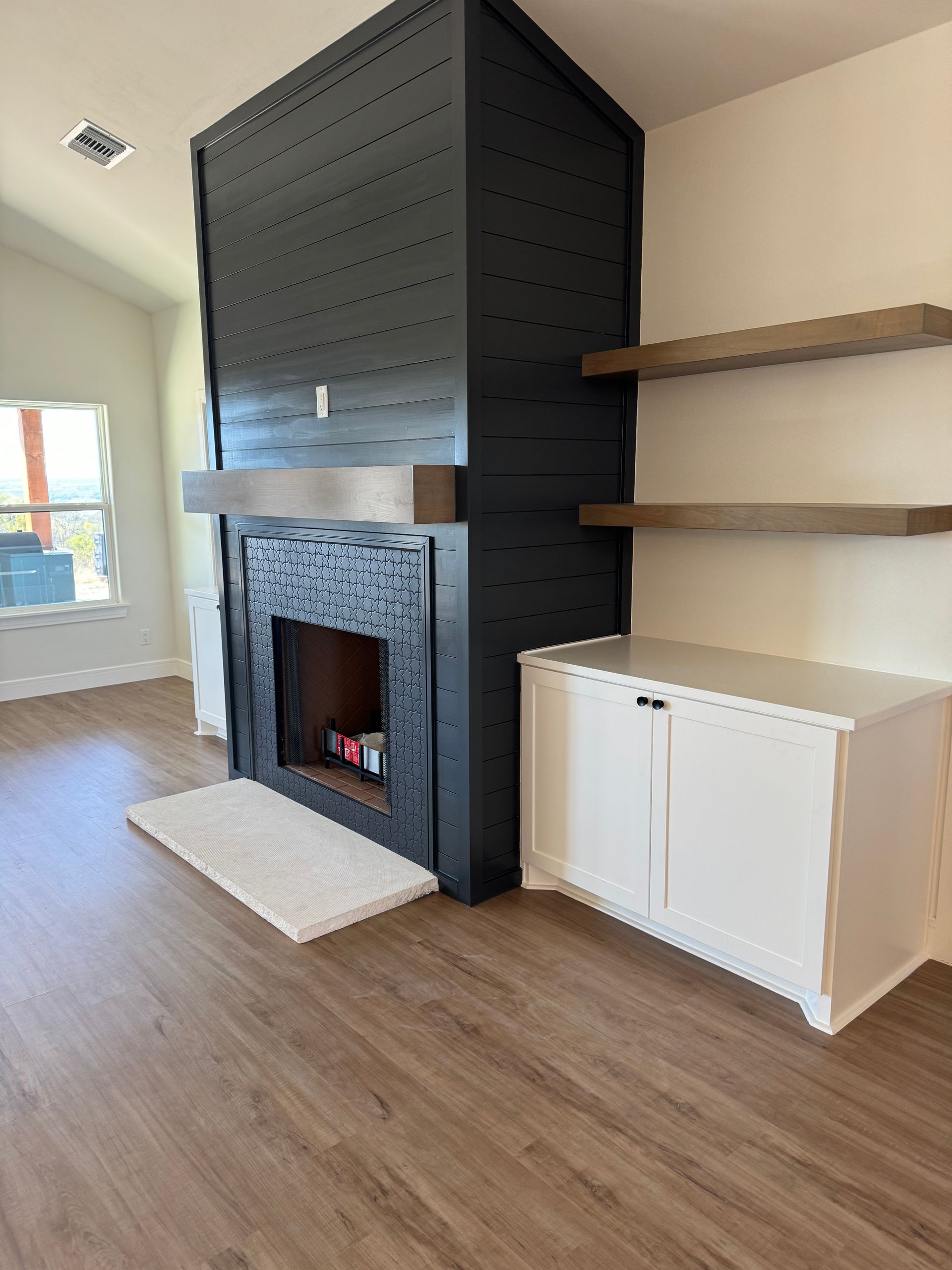 Black fireplace with white cabinet, wood shelves, and light brown floors.