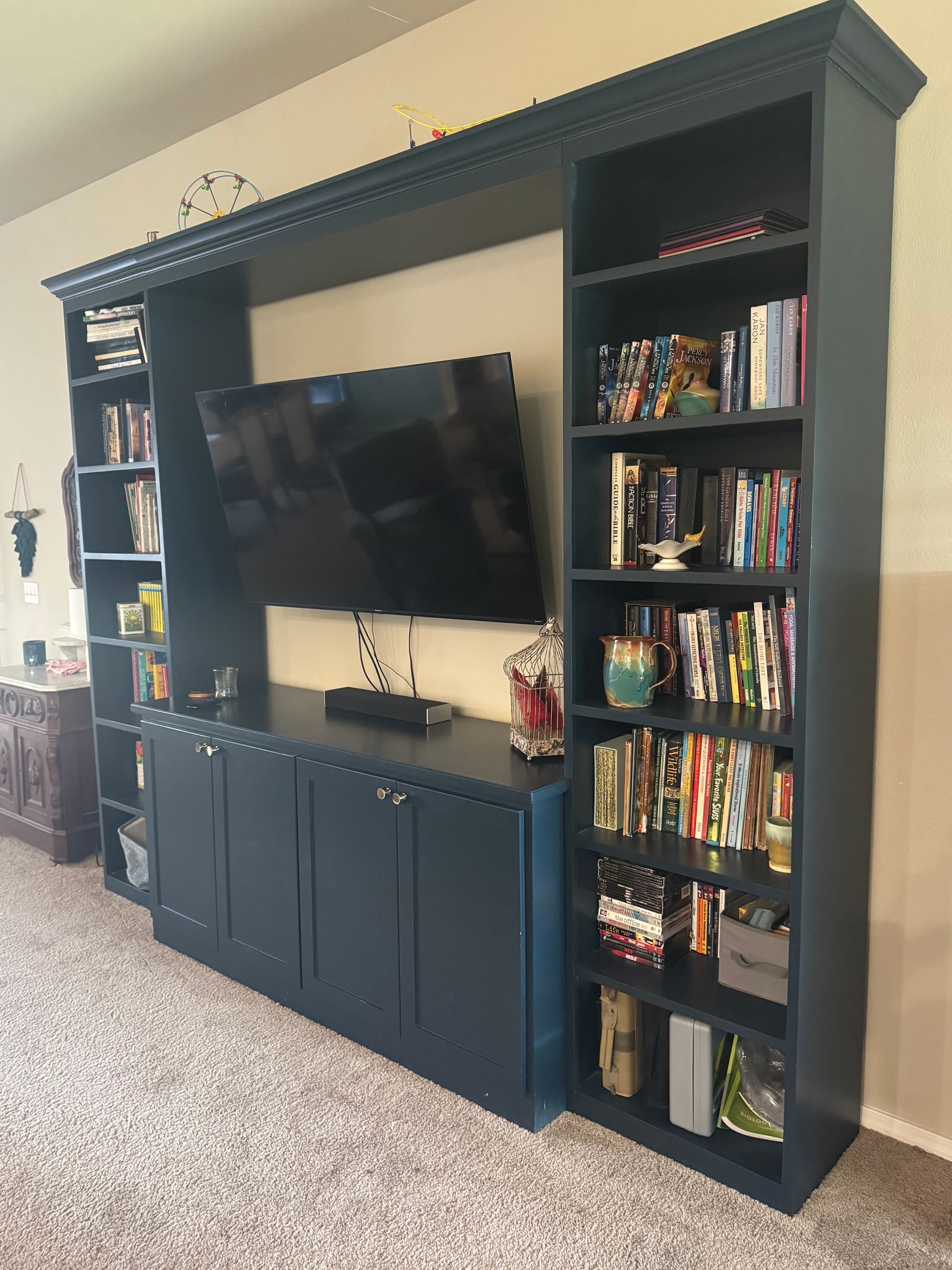 Dark blue built-in entertainment center with TV, storage cabinets, and bookshelves against a beige wall.