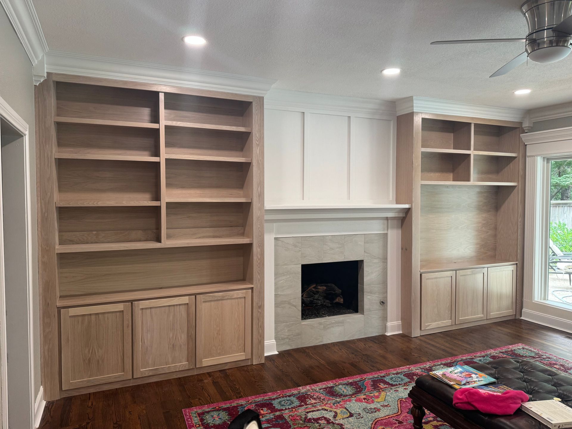 Built-in wooden bookshelves flank a fireplace in a living room; dark wood floor, white trim, rug.