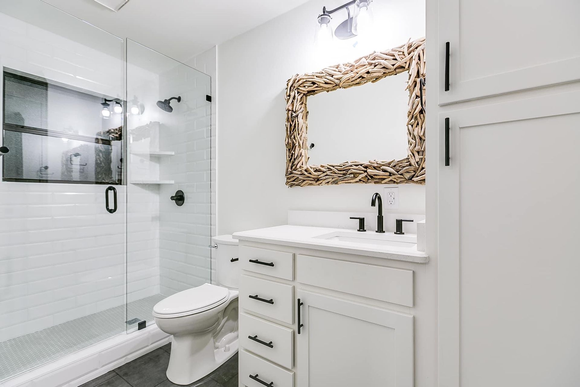 White bathroom with glass shower, driftwood mirror, and black accents.