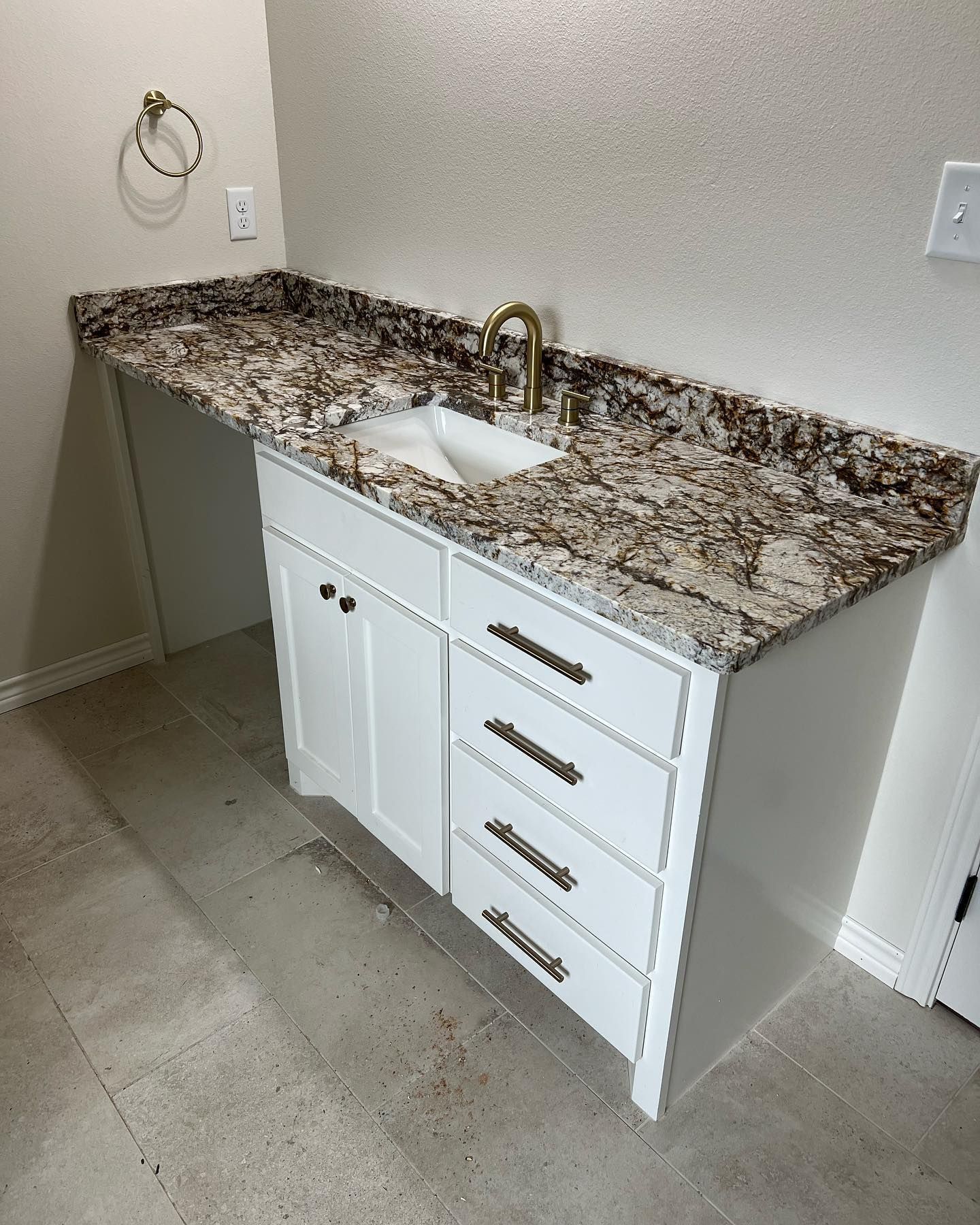 White bathroom vanity with granite countertop, gold faucet, and a white sink.