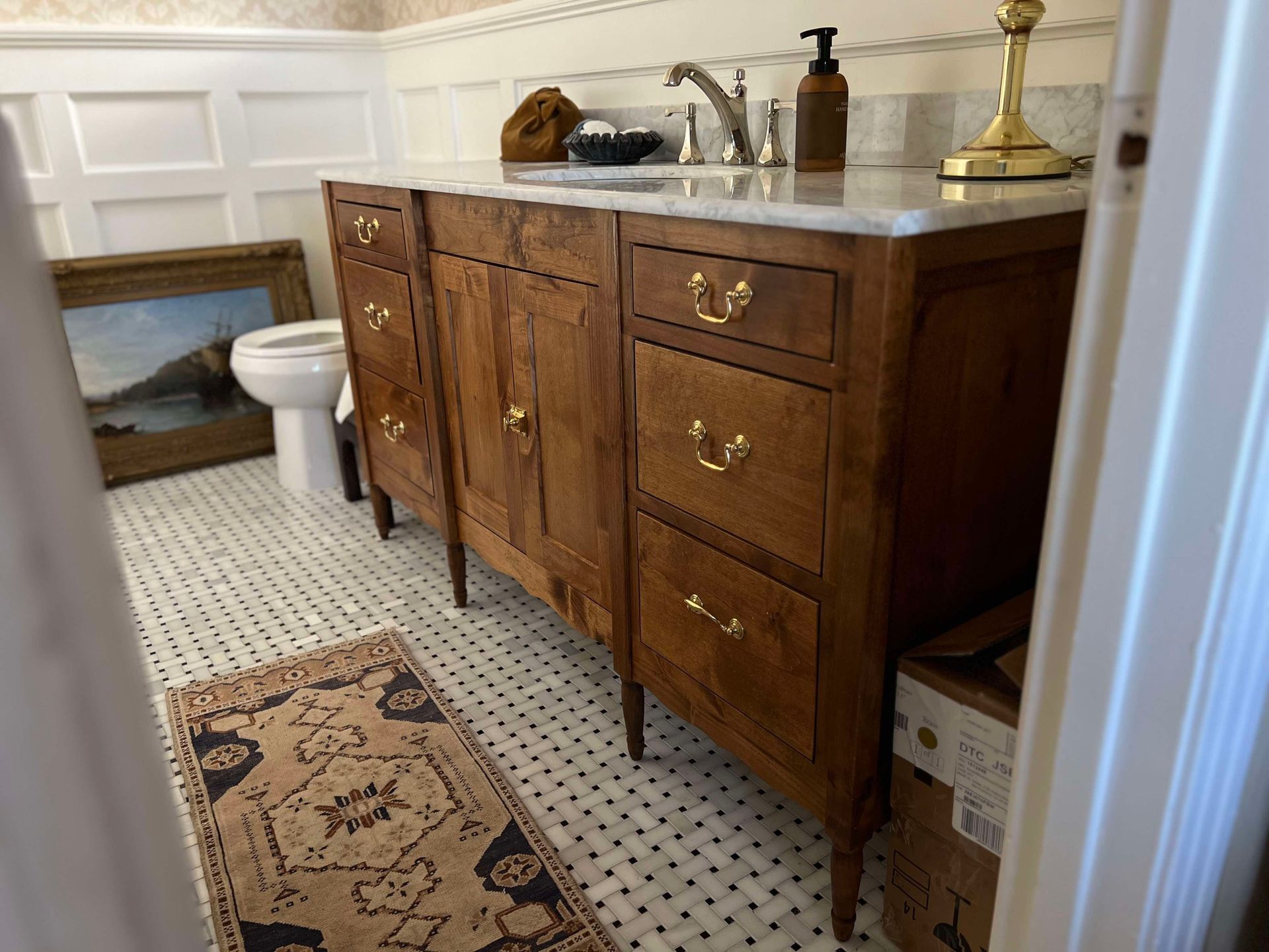 Bathroom with wood vanity, marble countertop, and patterned rug. White tiled floor and paneled walls.