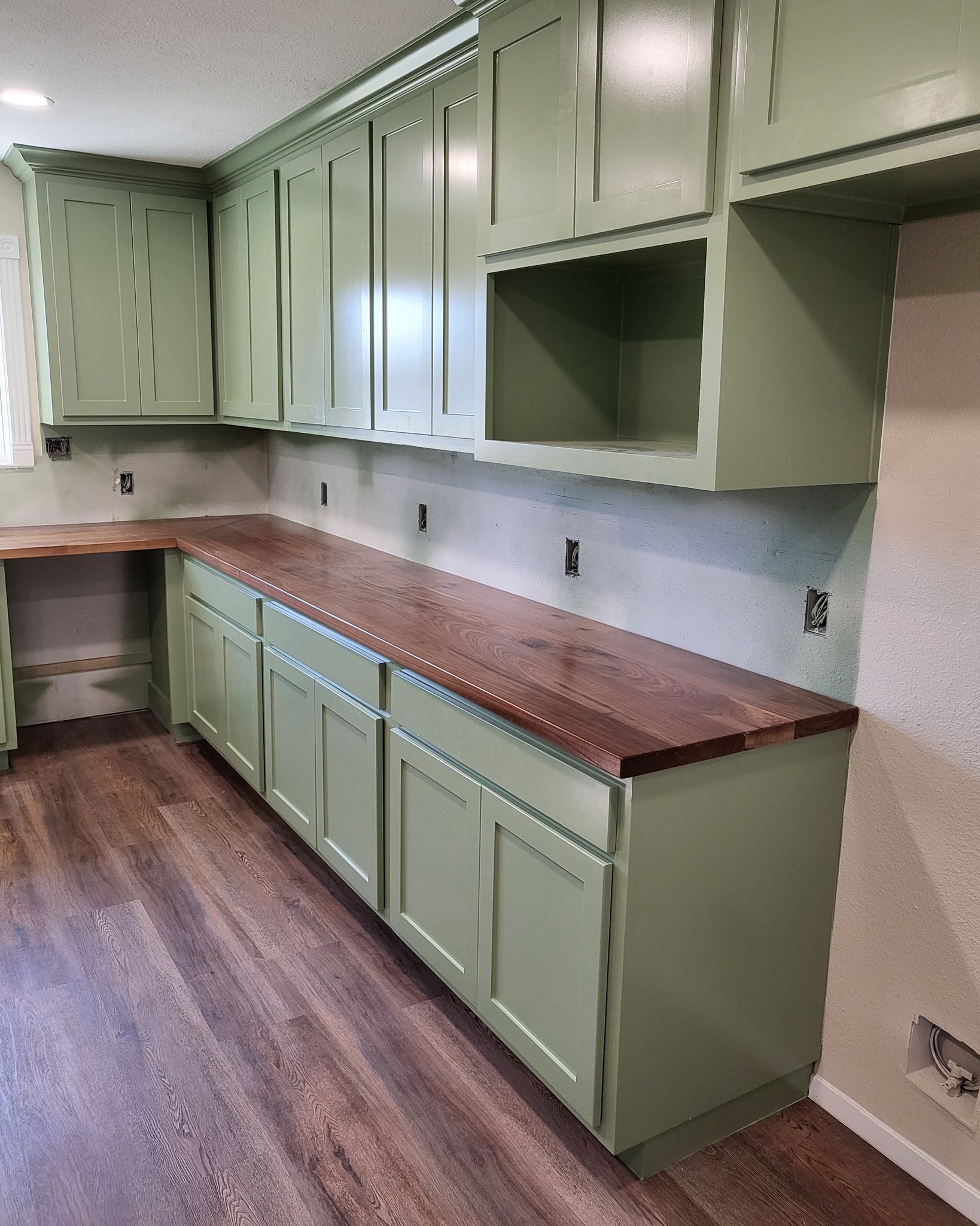 Green kitchen cabinets with wooden countertops and a brown floor.
