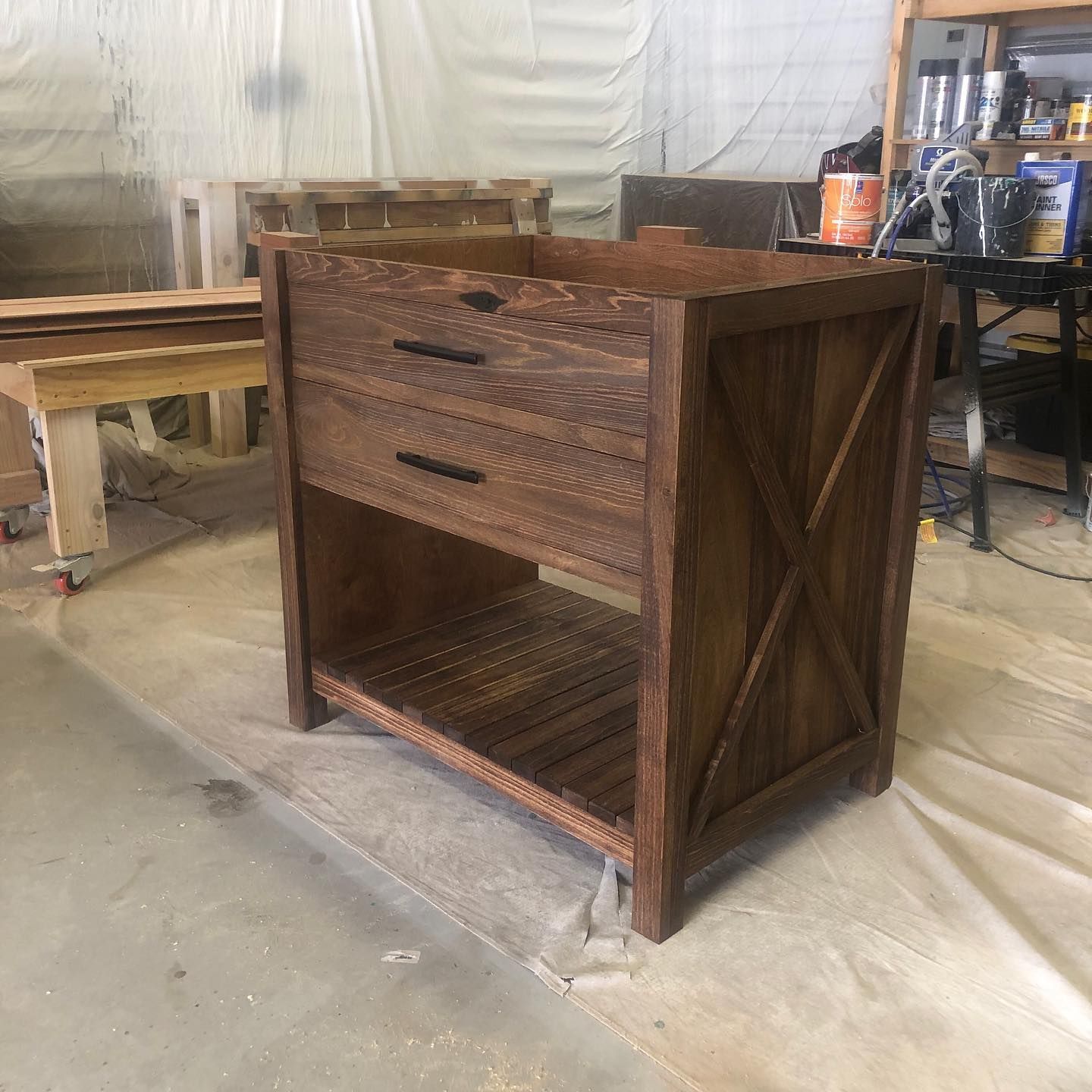 Wooden bathroom vanity with drawer and shelf, brown stain, X-shaped side supports.