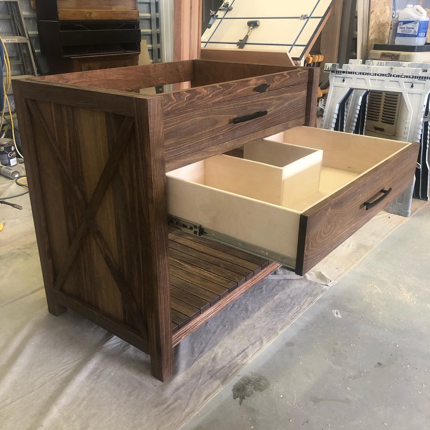 Wooden bathroom vanity with two drawers, one open, in a workshop.