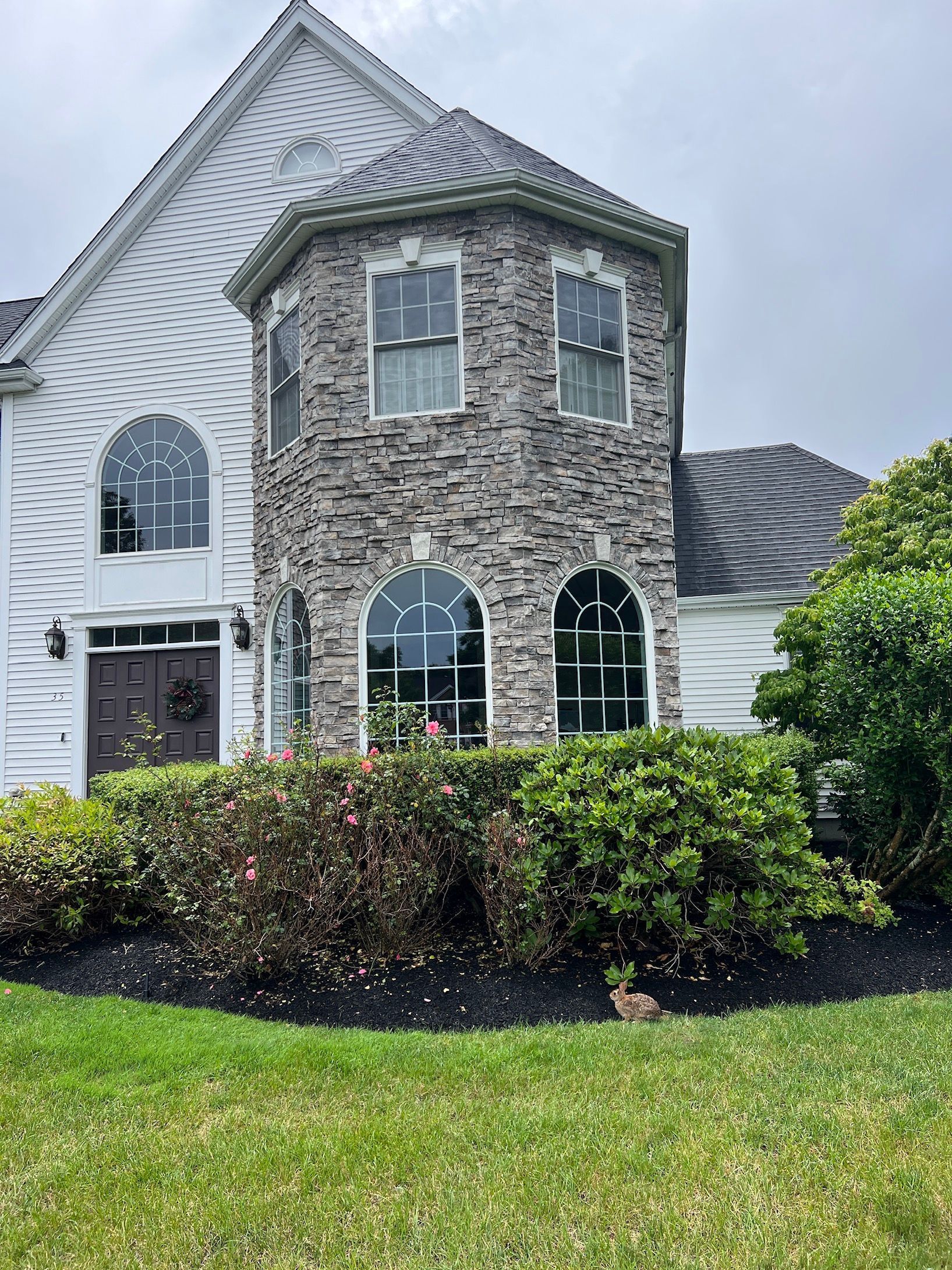 a large white house with a stone facade and a lot of windows is sitting on top of a lush green lawn.