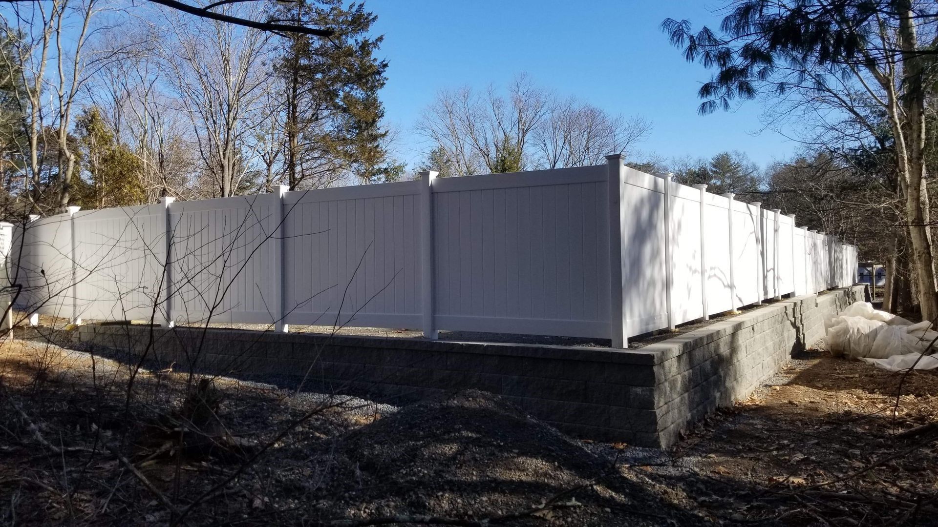 a white fence is surrounding a concrete base in the woods.