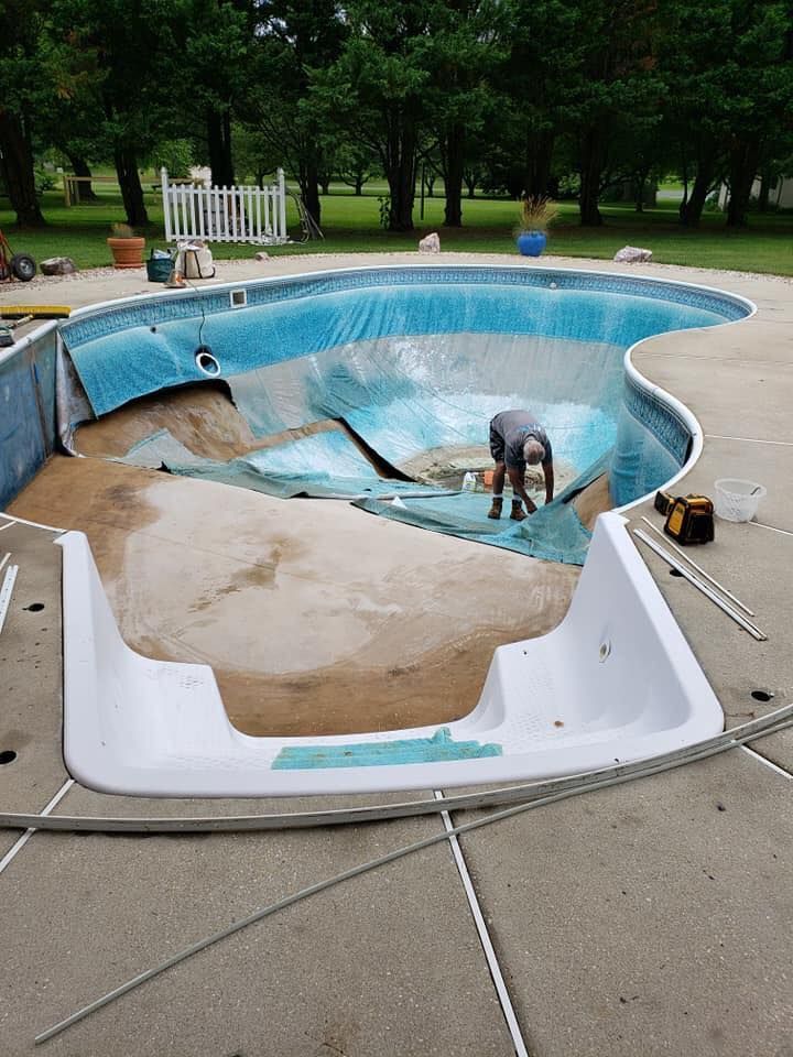 Partially drained backyard pool with a damaged liner and a person working inside