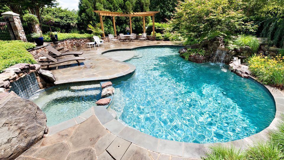 Backyard pool with waterfall, stone patio, lounge chairs, and garden landscaping
