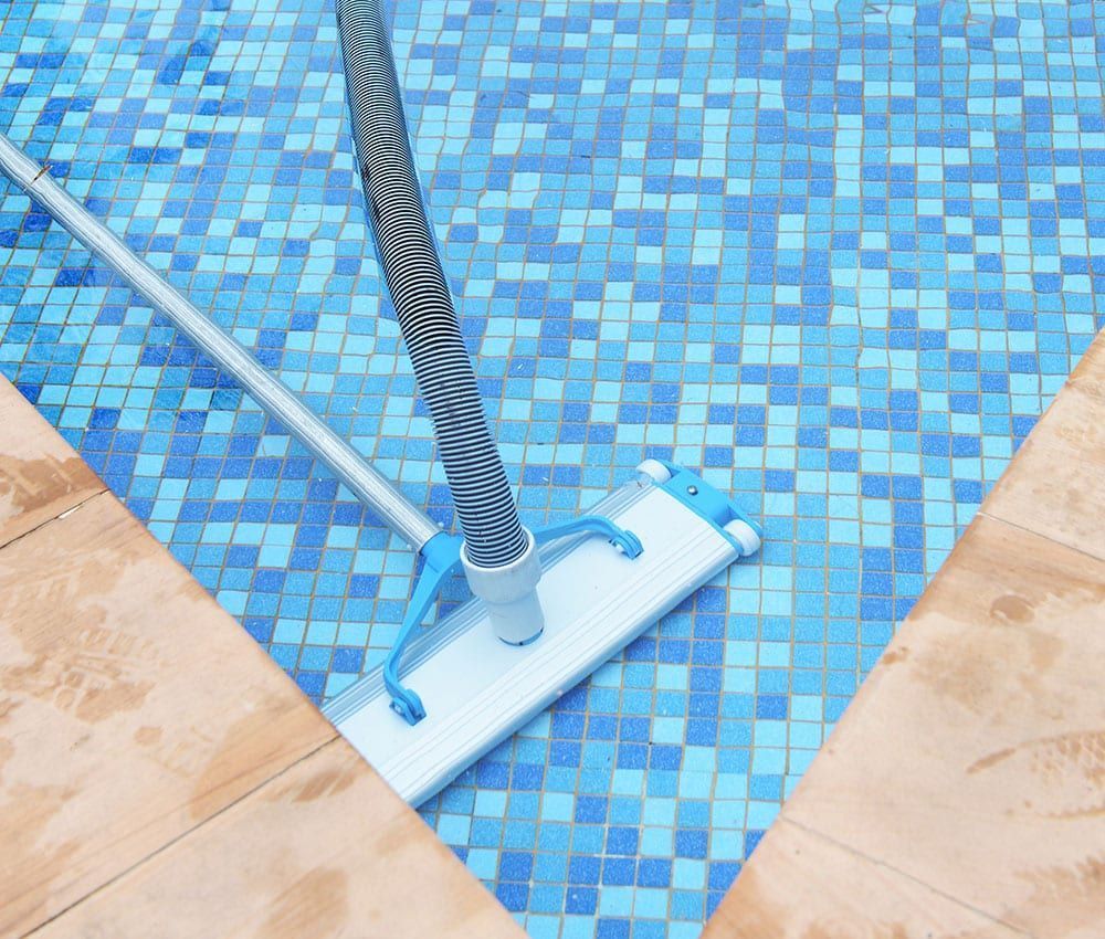 Pool floor cleaner on blue tiled pool deck, next to a striped vacuum hose
