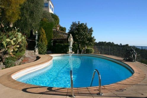 Curved backyard pool with blue water, wood deck, and garden views under a clear sky