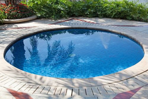 Round blue swimming pool surrounded by stone patio and lush greenery