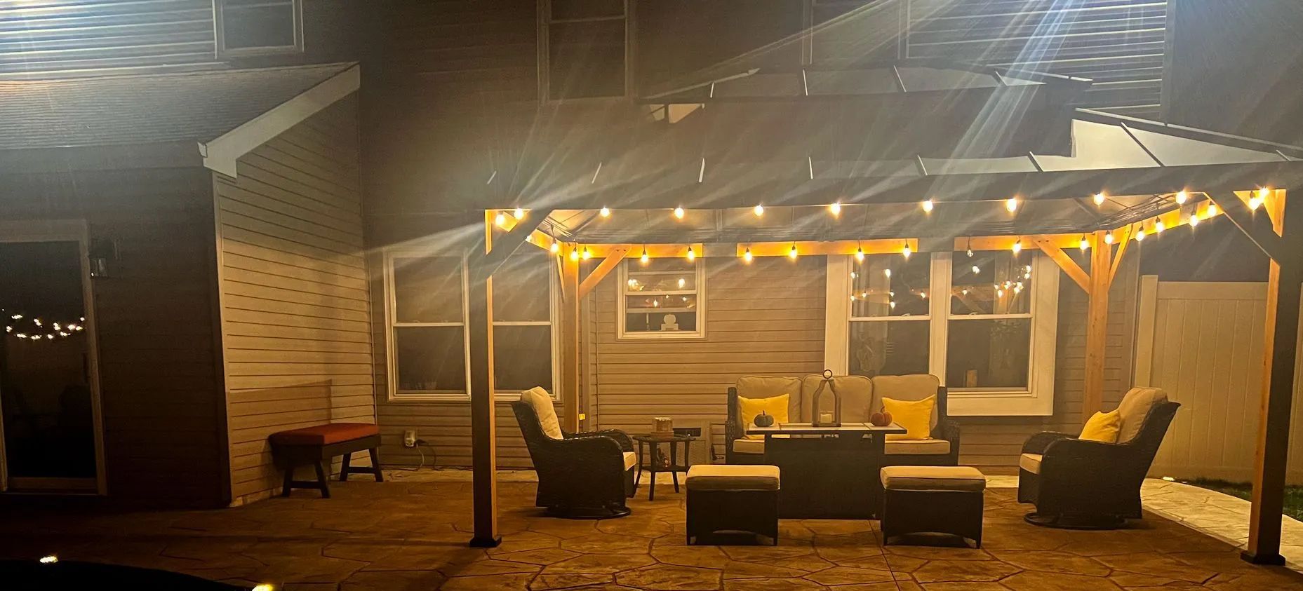 A patio with a pergola and lights at night.