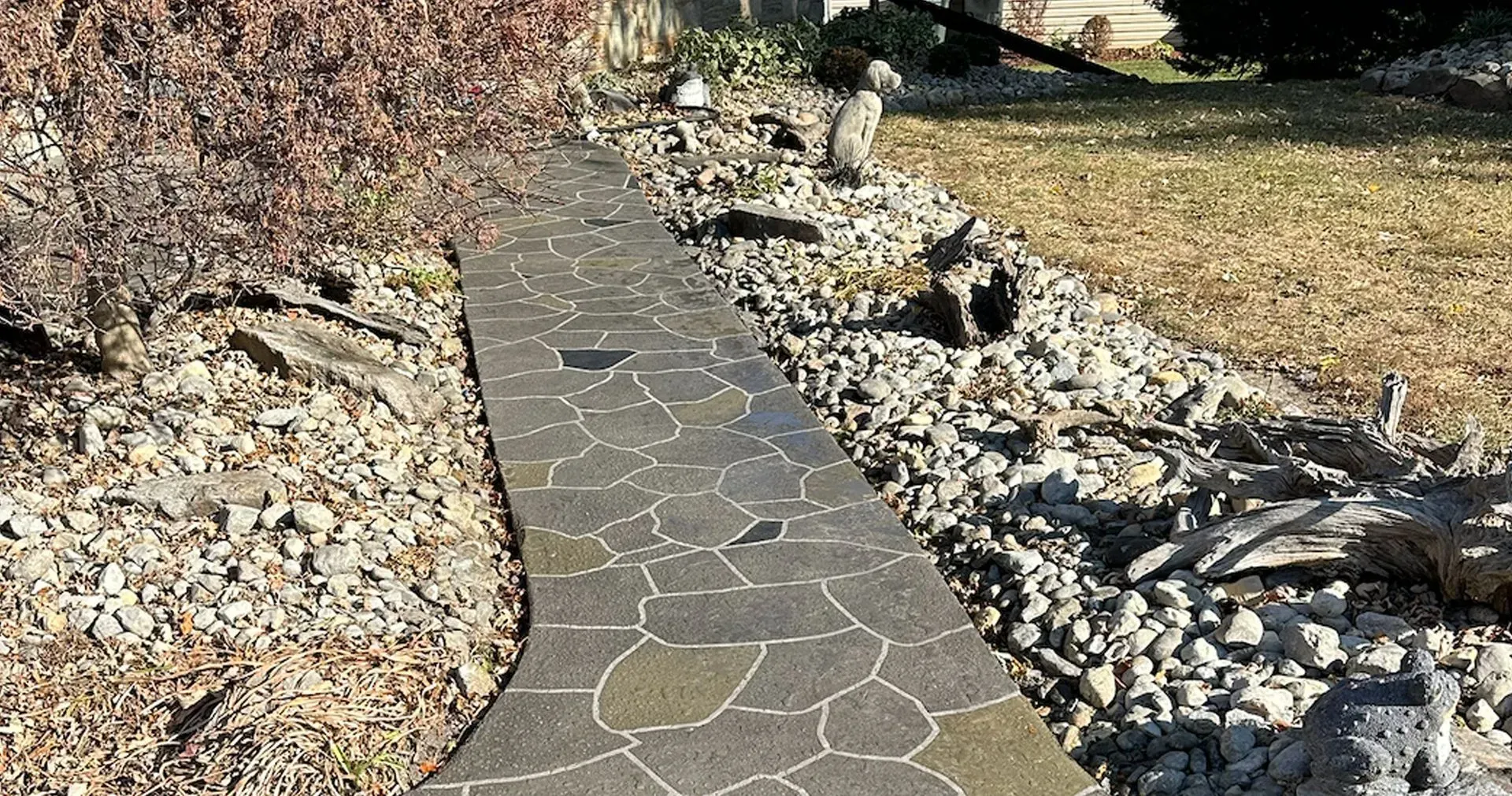 A stone walkway leading to a house surrounded by rocks and grass.
