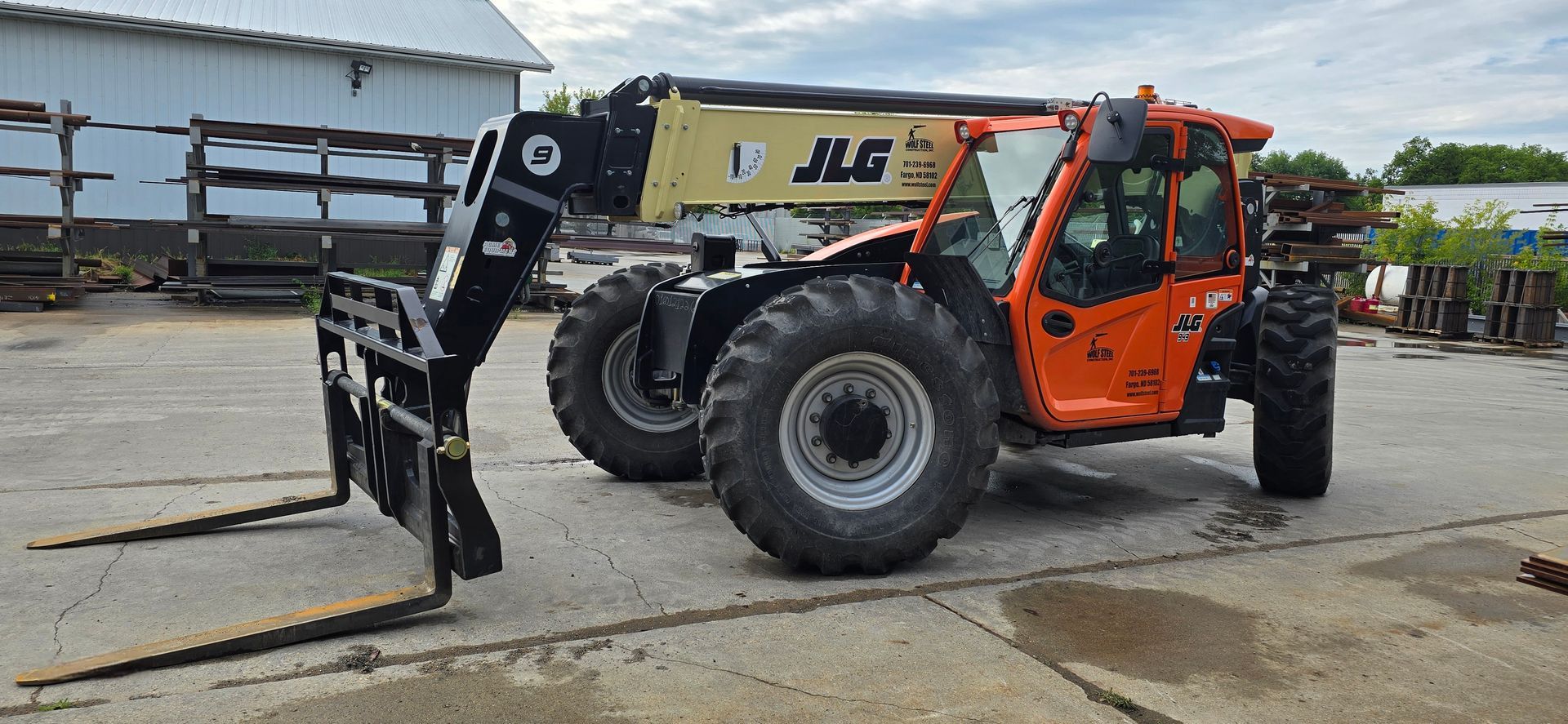 A tractor with a forklift attached to it is parked in a parking lot.