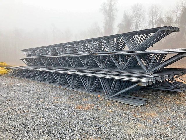 A stack of metal beams sitting on top of each other on a gravel road.