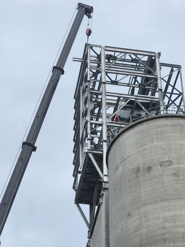 A crane is lifting a metal structure on top of a silo