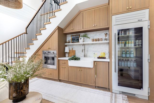 A kitchen with wooden cabinets and a refrigerator under the stairs.