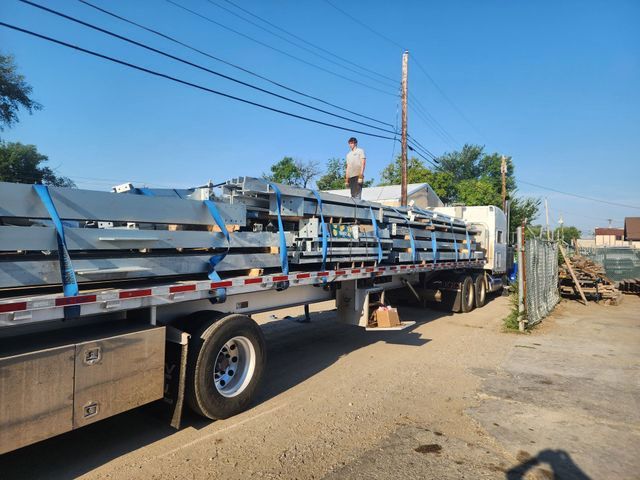 A man is standing on top of a semi truck loaded with metal sheets