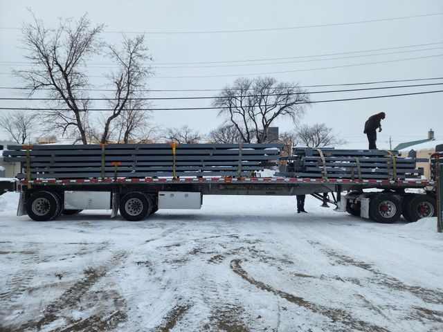 A semi truck is carrying a stack of pipes in the snow.