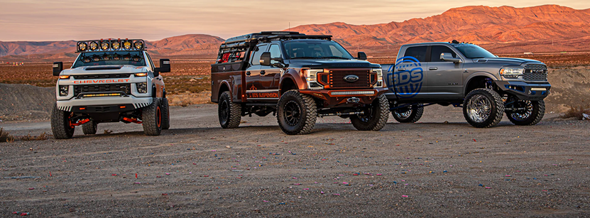 Three trucks with lift kits are parked next to each other in the desert
