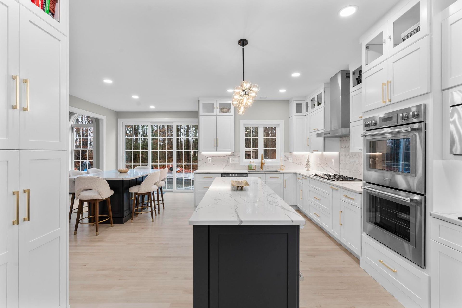 A modern kitchen features white cabinetry, a dark central island with a marble countertop, and stainless steel appliances.