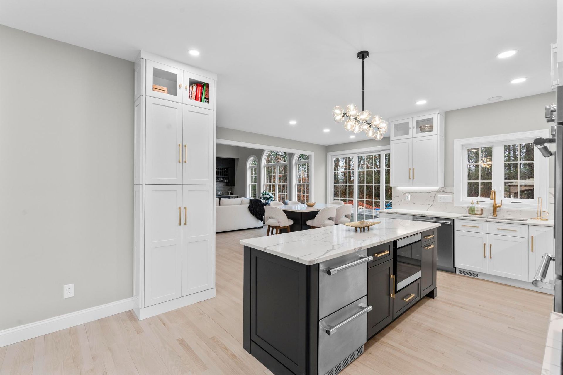 Modern kitchen with a dark-colored island, white cabinetry, granite countertops, and light hardwood floors.