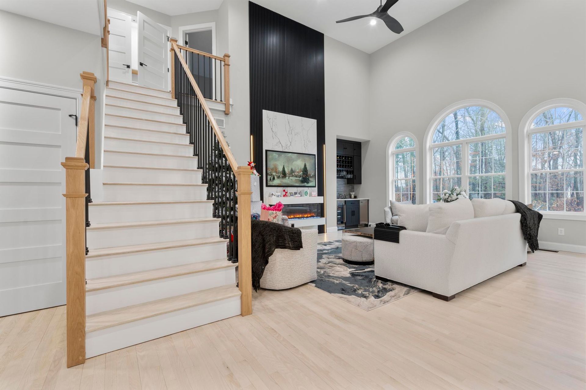 Modern open-plan living room with white staircase, black accent wall, fireplace, and light wood flooring.