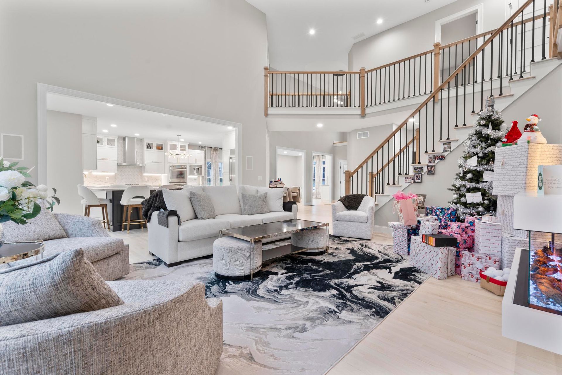 A spacious, modern living room with a large white sectional, a patterned rug, a fireplace, and a decorated Christmas tree.