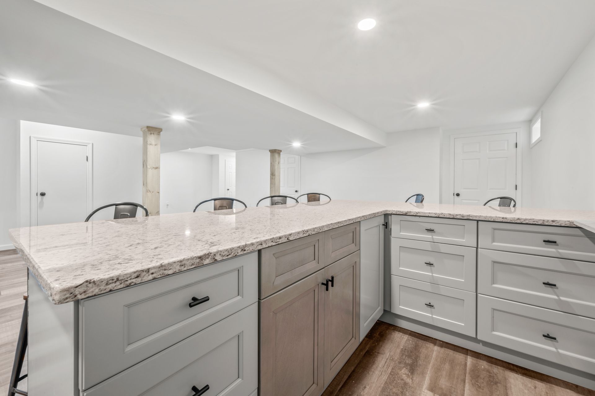 A light gray kitchen island with a speckled granite countertop in a white, finished basement with LVP flooring.