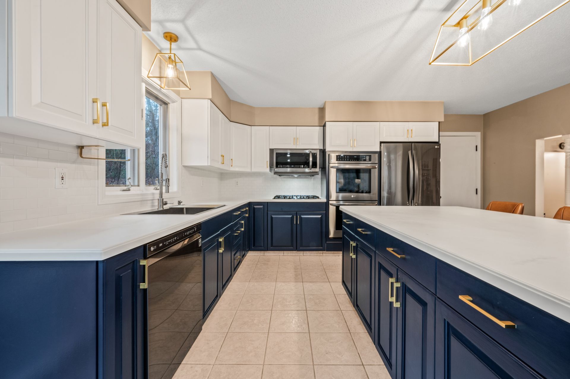 A kitchen with two-toned navy blue lower cabinets and white upper cabinets, stainless steel appliances, and an island.