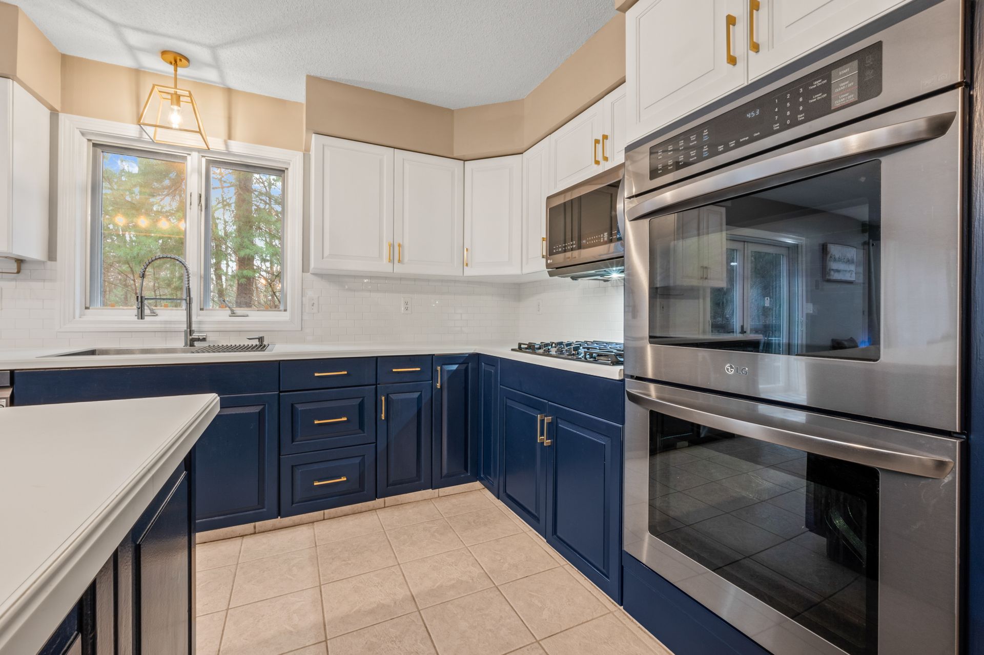 A kitchen with navy blue lower cabinets, white upper cabinets, stainless steel double ovens, and tiled flooring.