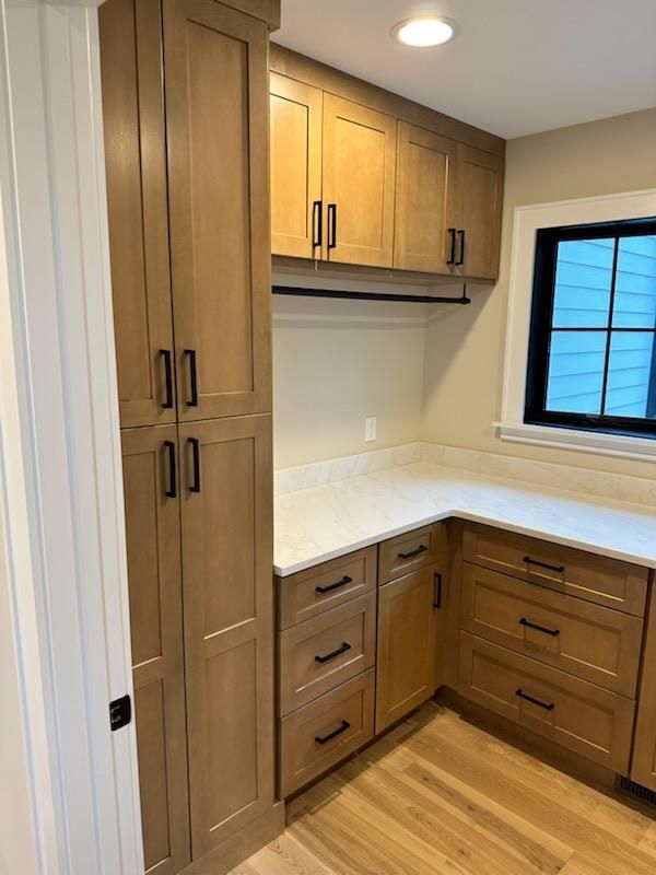 A custom-built wood pantry cabinet beside a matching counter with drawers and upper cabinets, under a small window.
