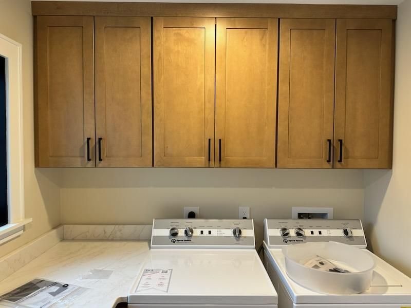 Light wood cabinets hang above a white washer and dryer in a laundry room.