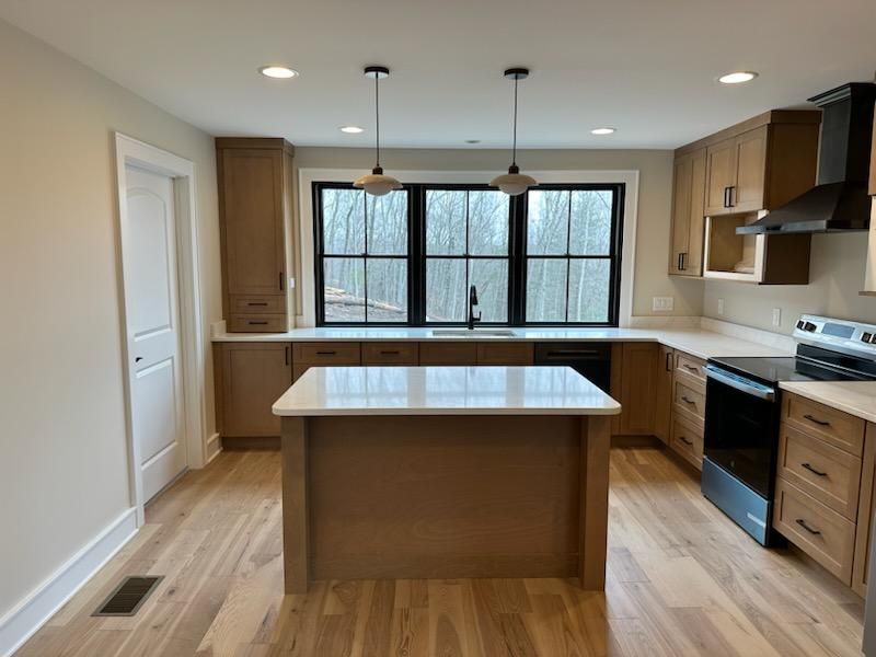 A modern kitchen with light wood cabinets, a white quartz island, black window frames, and stainless steel appliances.
